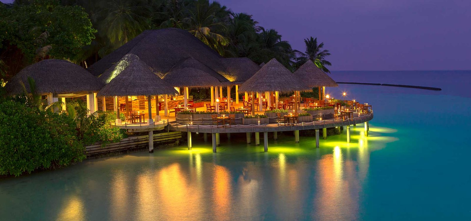 Overwater restaurant lit at night at Baros Maldives