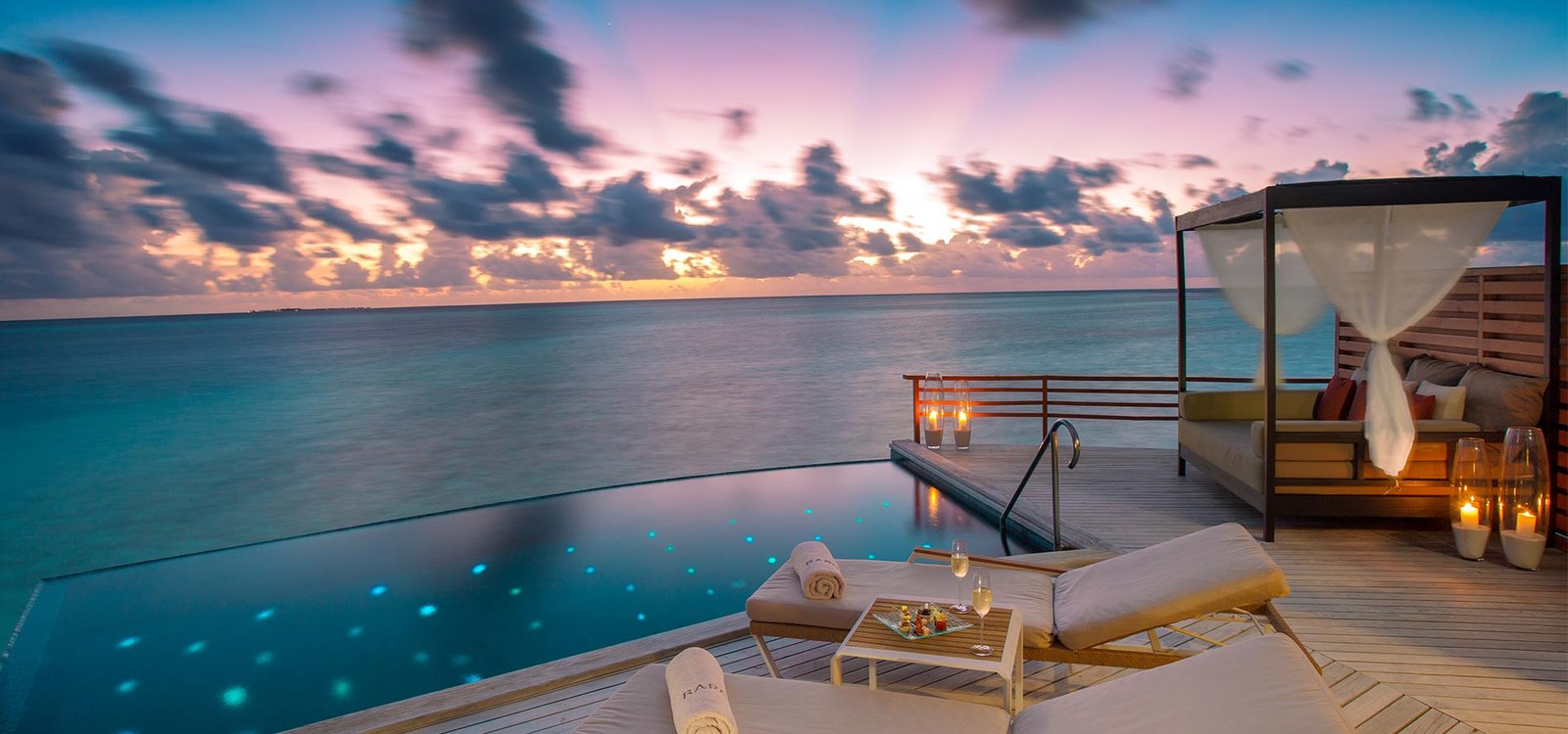 Overwater deck with a daybed at sunset at Baros Maldives