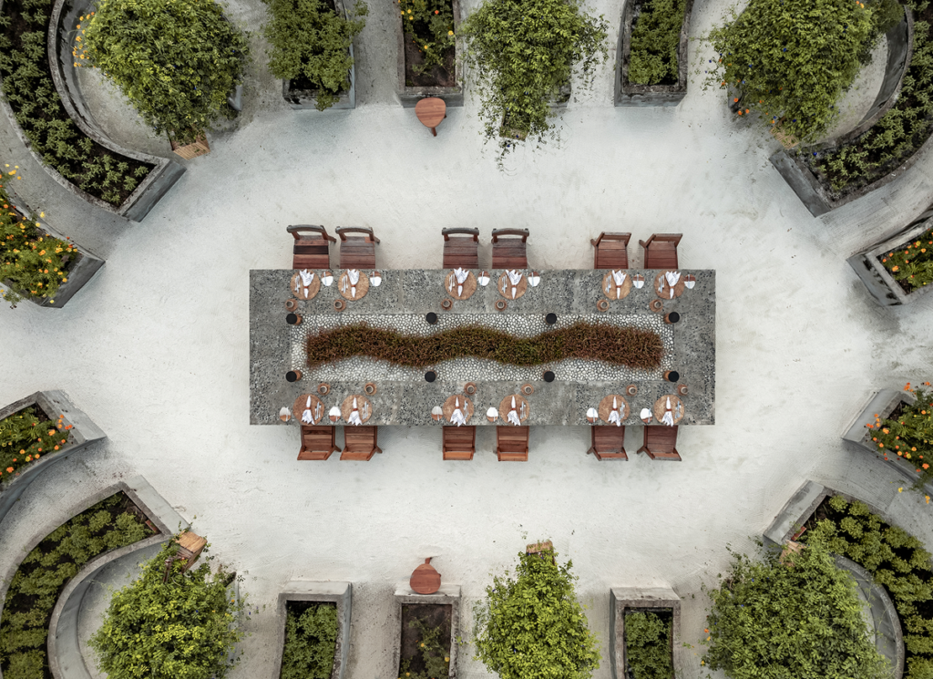 Aerial view of a long dining table set on the sand at Patina Maldives