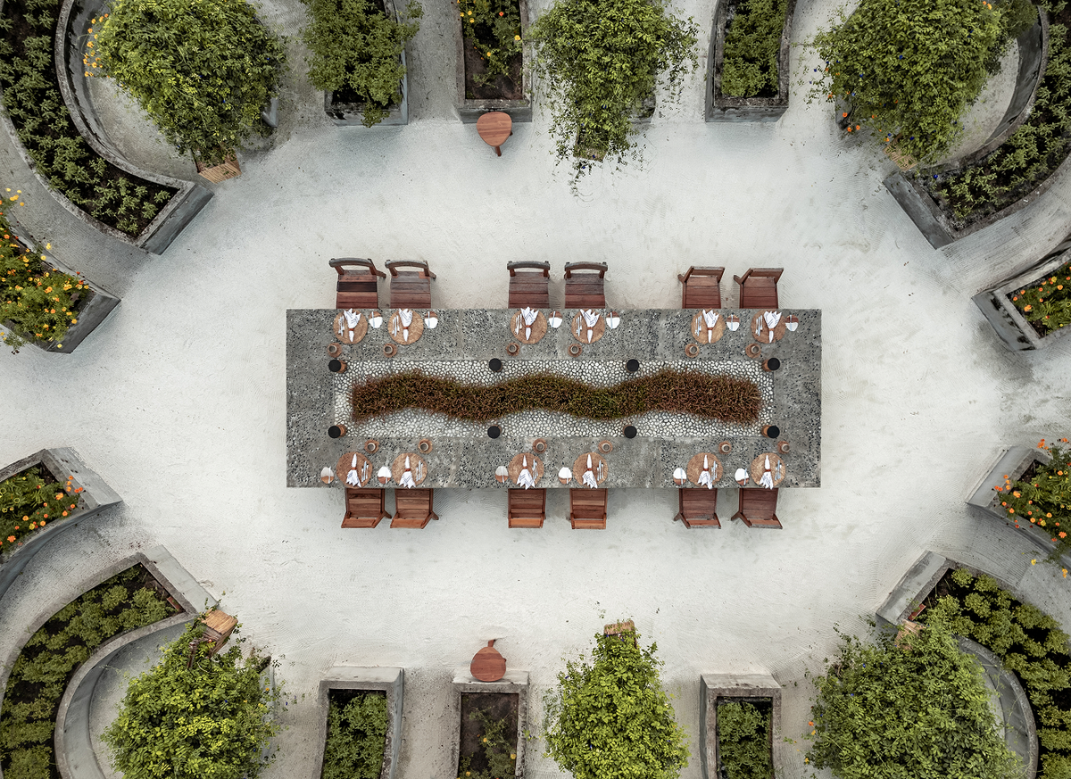 Aerial view of a long dining table set on the sand at Patina Maldives